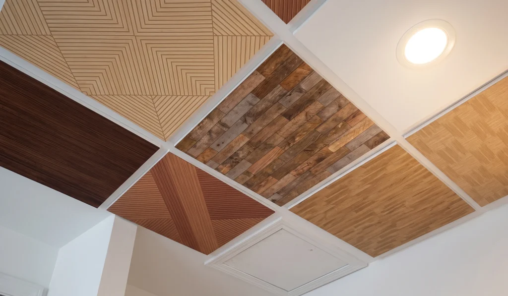 Decorative acoustic ceiling panels in mixed wood finishes and geometric patterns installed in a grid layout.