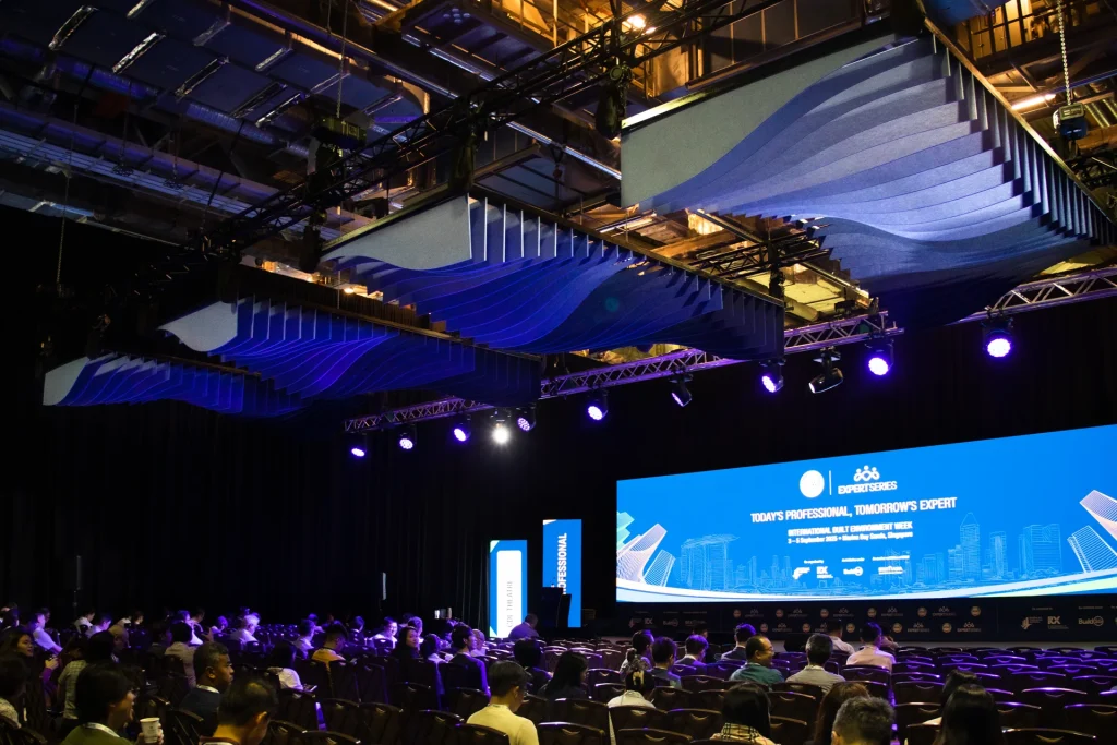 Blue gradient Klar™ acoustic ceiling baffles above a seated audience at the CDL Theatre, BEX Asia 2025 Singapore