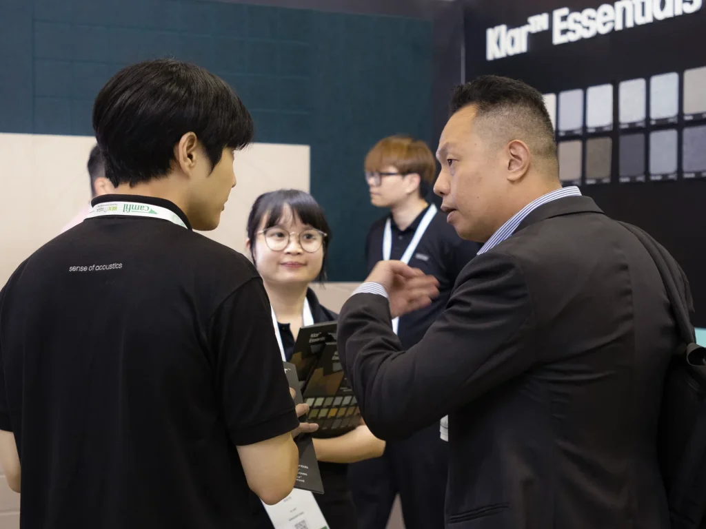 Klarist sharing Klar™ Essentials acoustic panel samples with a visitor at the Klar booth, BEX Asia 2025